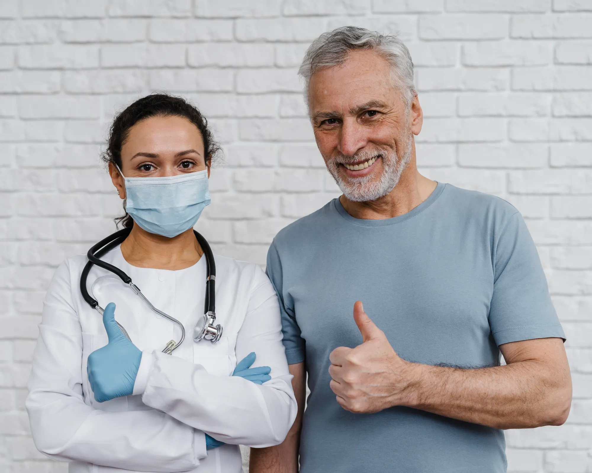 Doctora y paciente sonriendo y levantando el pulgar frente a una pared blanca