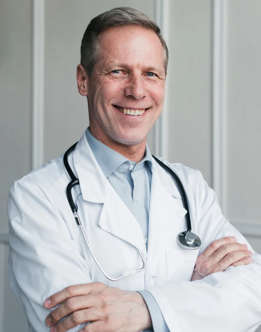 Médico de mediana edad sonriendo con brazos cruzados