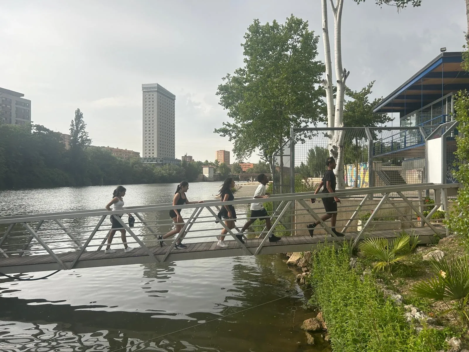 cinco personas jóvenes cruzan un puente pasarela sobre un río en Valladolid